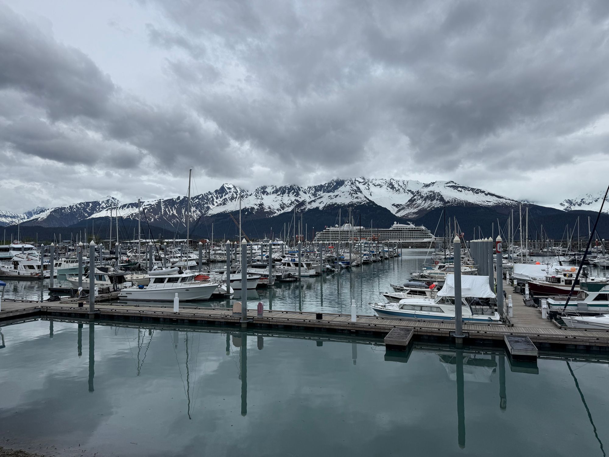 Scenic view of Seward Harbor with boats and snow-capped mountains under a cloudy sky.