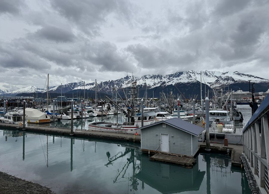 Scenic view of Seward Harbor with boats and snowcapped mountains under cloudy skies.