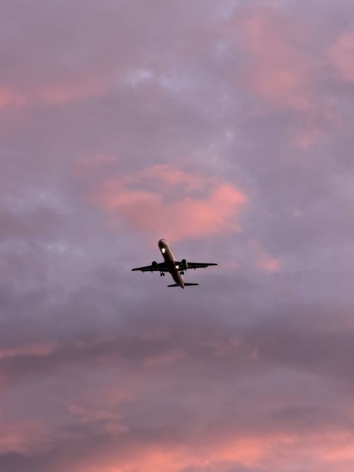 Free An airplane flies gracefully against a backdrop of a beautiful pink and purple sunset sky, capturing the essence of travel and adventure. Stock Photo