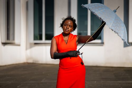 Free Stylish woman holding a parasol in sunlight, wearing red dress and gloves. Stock Photo