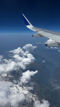 Breathtaking aerial view of the Himalayas from an airplane with wing visible, capturing clouds and snow-capped peaks.