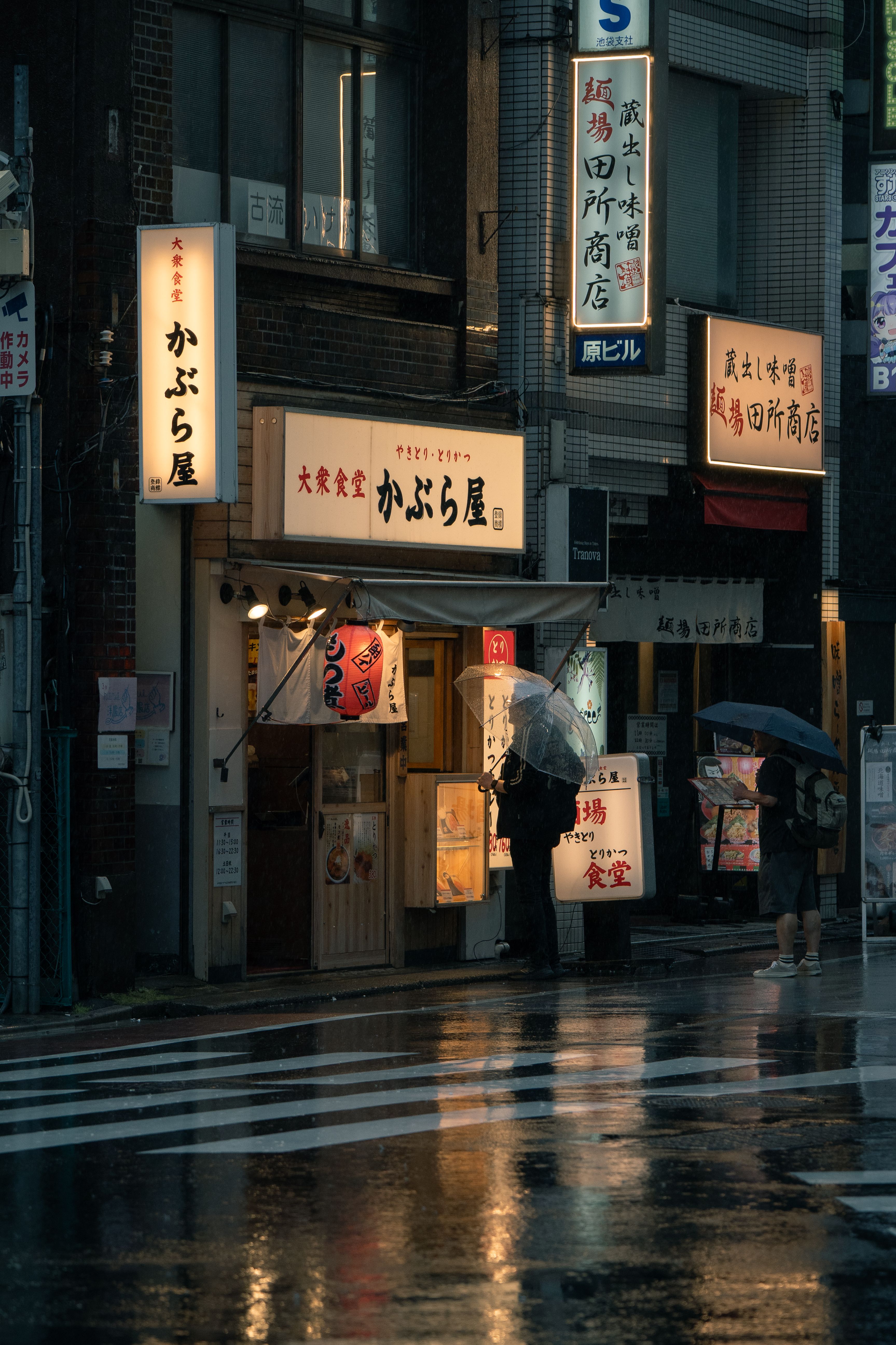雨の降る日本の商店街。傘をさした人が店先に立っている