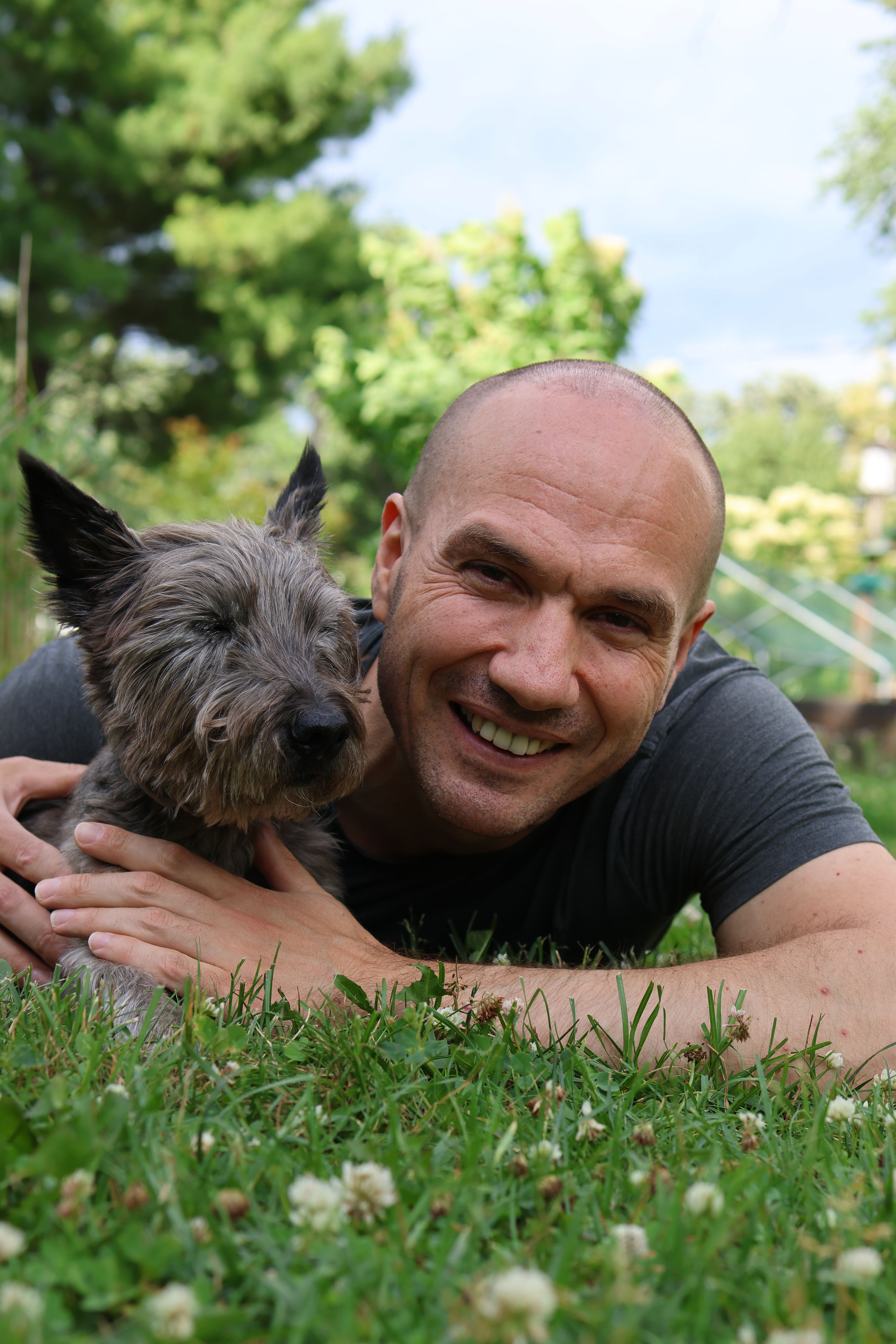 A joyful moment between a man and his Cairn Terrier in a sunny garden setting.