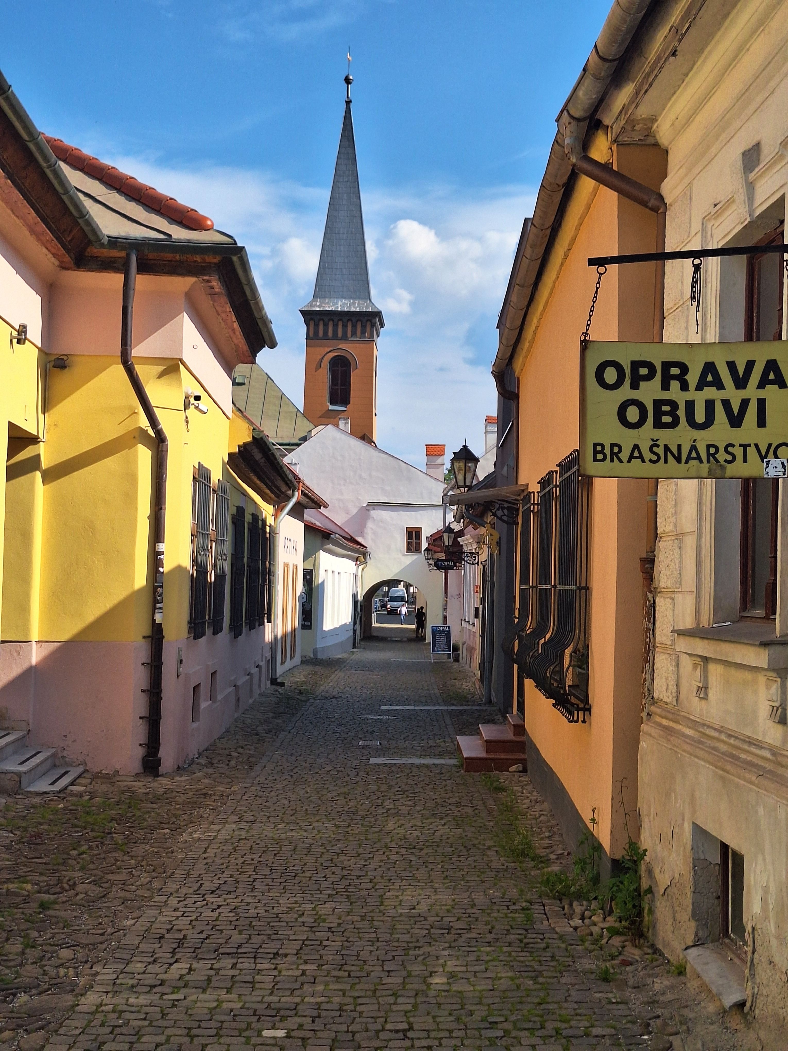 Picturesque European alley with colorful buildings and a distant church tower.