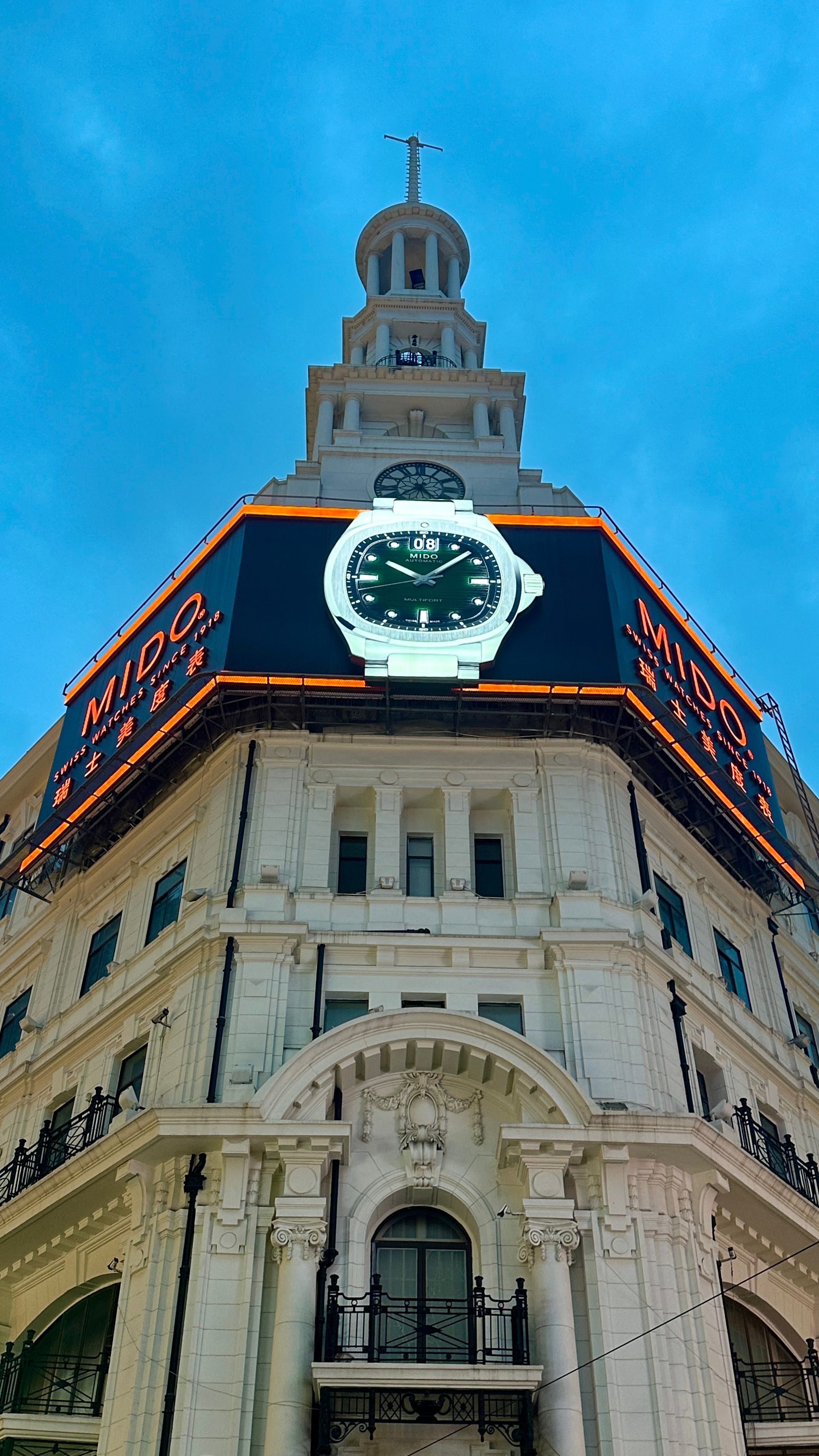 View of a historic building in Shanghai featuring a large outdoor watch display against a blue sky.