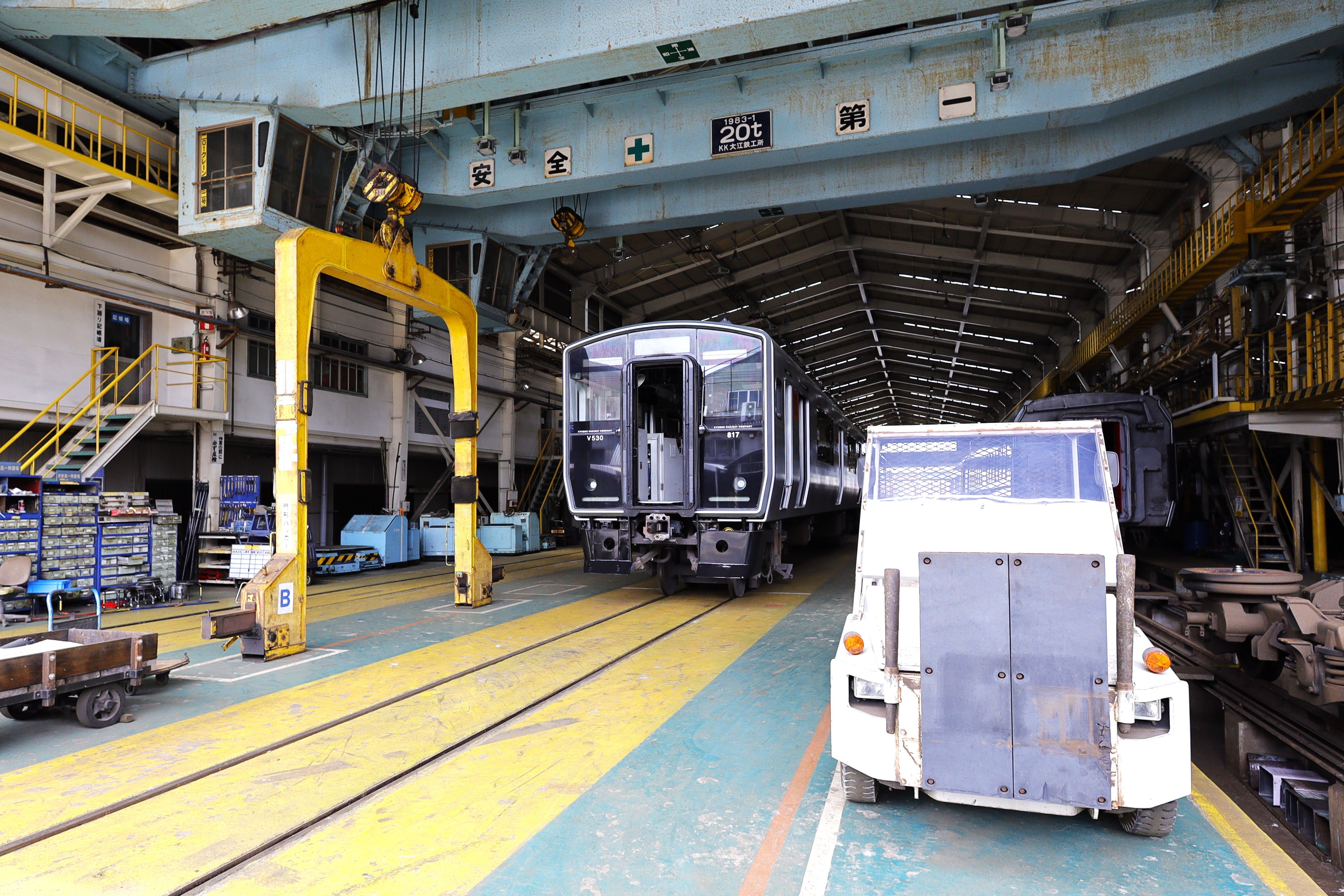 日本の北九州市にある鉄道車両整備施設の内部写真。列車と整備設備が写っている。