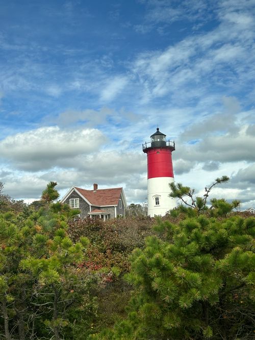 Free Dramatic shot of Nauset Lighthouse surrounded by greenery and clouds in Eastham, MA. Stock Photo