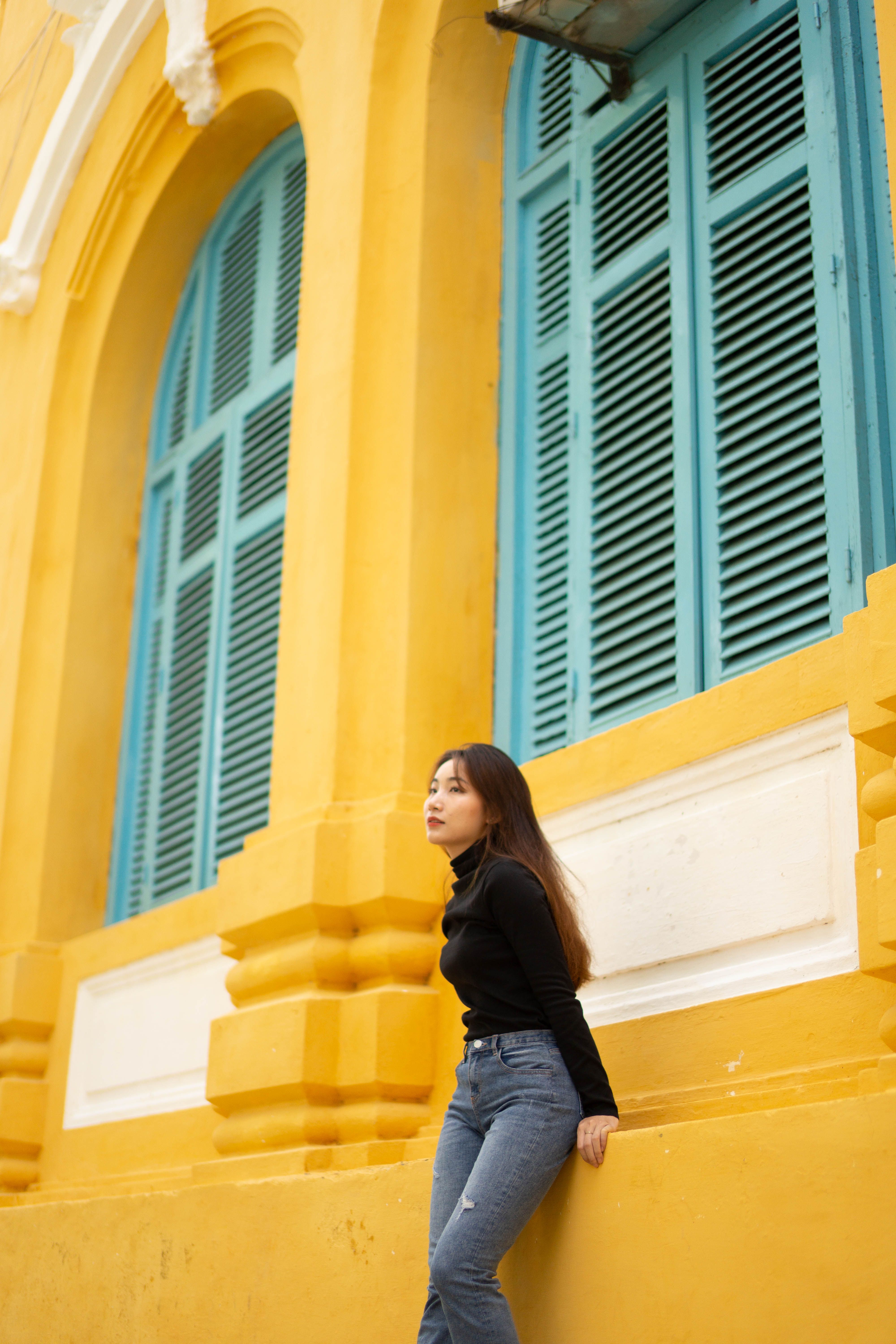 Portrait of a stylish woman in front of a vibrant yellow and teal building facade.