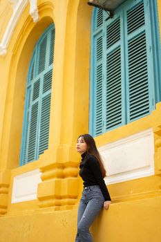 Portrait of a stylish woman in front of a vibrant yellow and teal building facade.