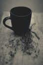 From above of composition of black mug near dry sprigs with thin stems and tiny leaves tied with ribbon on wooden surface with crack