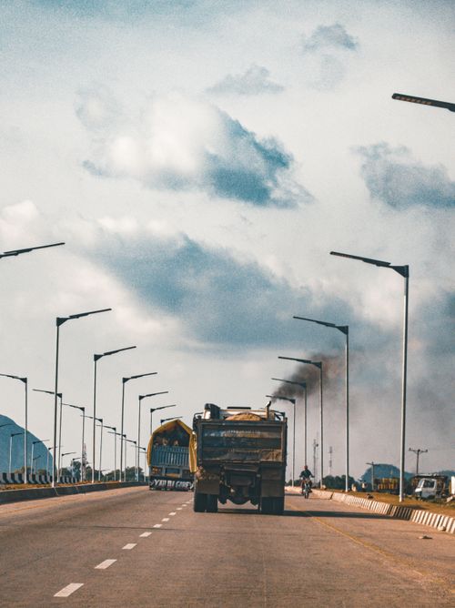 Free A bustling highway scene in Abuja, Nigeria, with trucks and smoky exhaust under a cloudy sky. Stock Photo