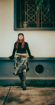 Fashionable woman in modern outfit leaning on urban wall, exuding confidence.