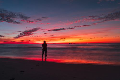 Free A person stands silhouetted against a vibrant sunset on a beach in Quảng Trị, Vietnam. Stock Photo