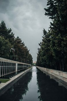 A serene, rainy vista of Martyrs' Lane in Baku, Azerbaijan, featuring lush trees and reflective pavement.