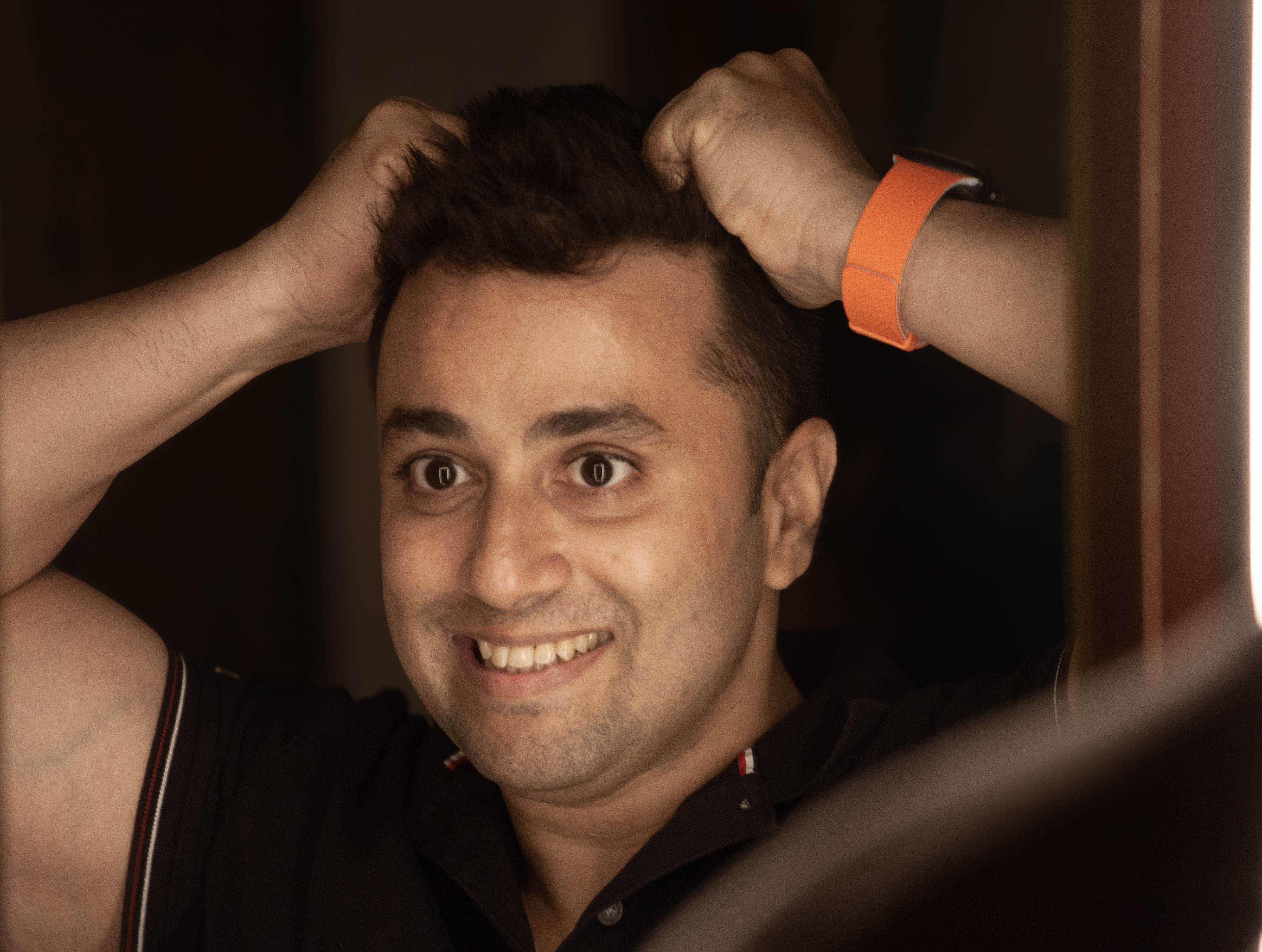 Smiling man adjusting his hair while wearing a casual shirt and smartwatch indoors.