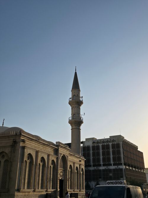 Free Mosque minaret reaching skyward at sunset, with surrounding architecture in warm glow. Stock Photo
