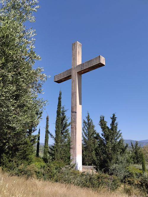Free A tall wooden cross surrounded by lush greenery under a clear blue sky in daylight. Stock Photo