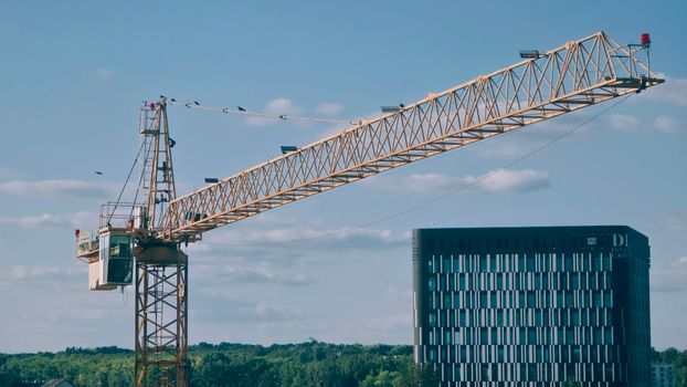 A tall construction crane against a blue sky with a modern building backdrop.