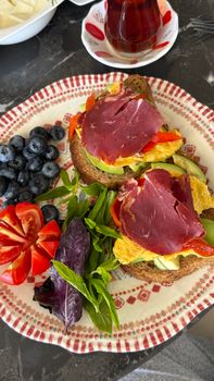 Colorful open-faced sandwich with vibrant garnishes on ornamental plate.