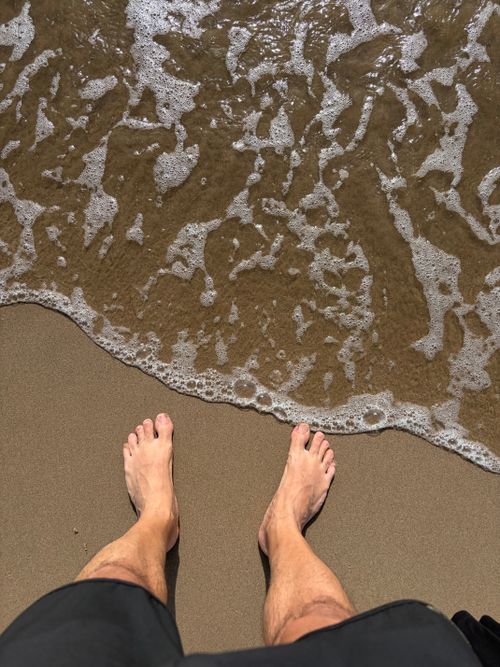 Free Bare feet standing on a sandy beach with ocean waves gently washing ashore. Stock Photo