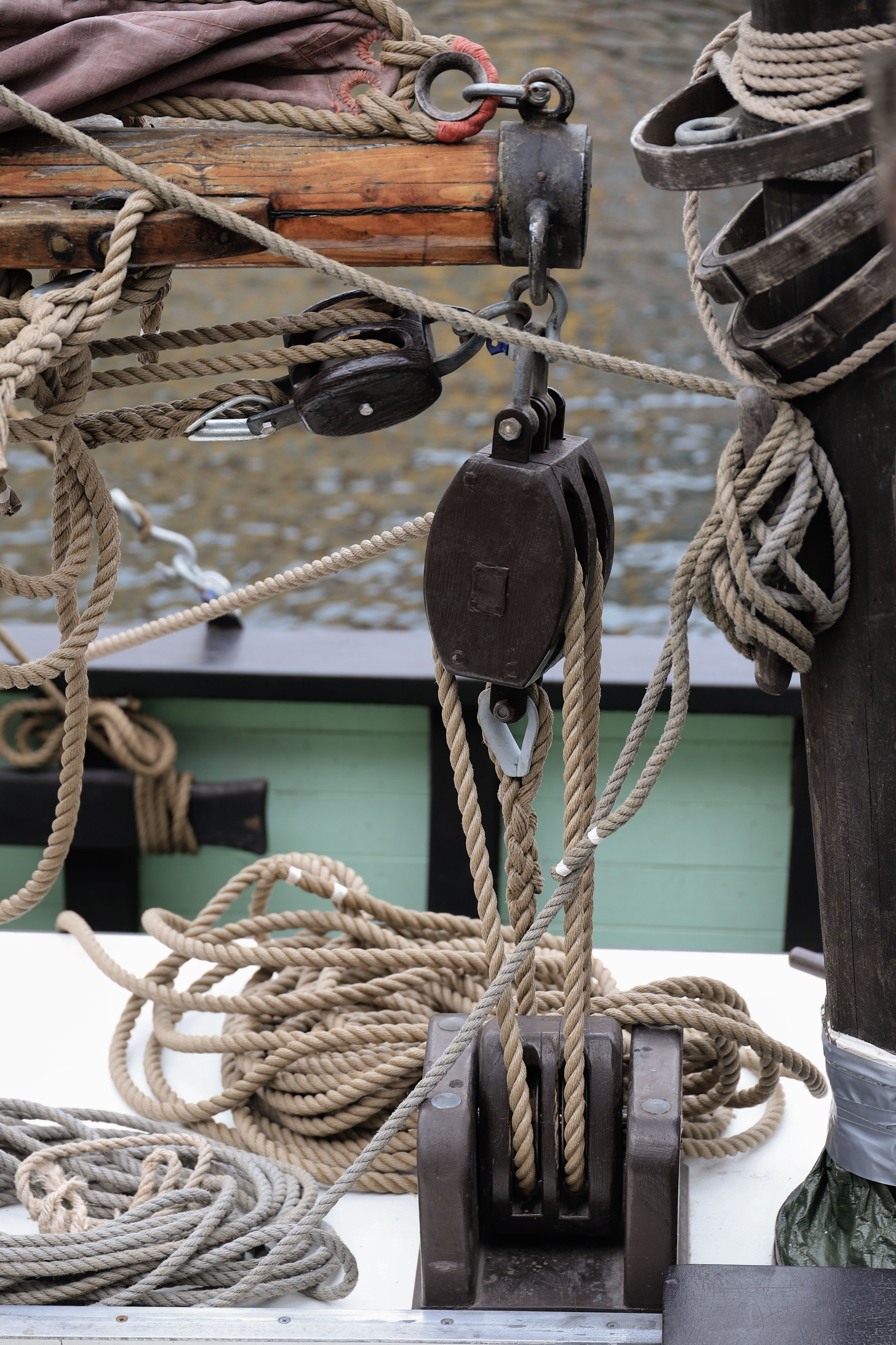 Close-up of wooden sailing ship equipment in Copenhagen harbor, featuring ropes and pulley blocks.