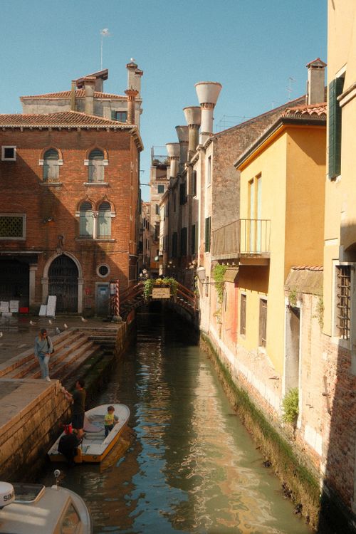 Free Picturesque Venetian canal surrounded by historic buildings and a small boat, capturing the essence of Venice. Stock Photo