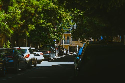 Free Sunny residential street in Tbilisi with parked cars and lush green trees casting shadows. Stock Photo