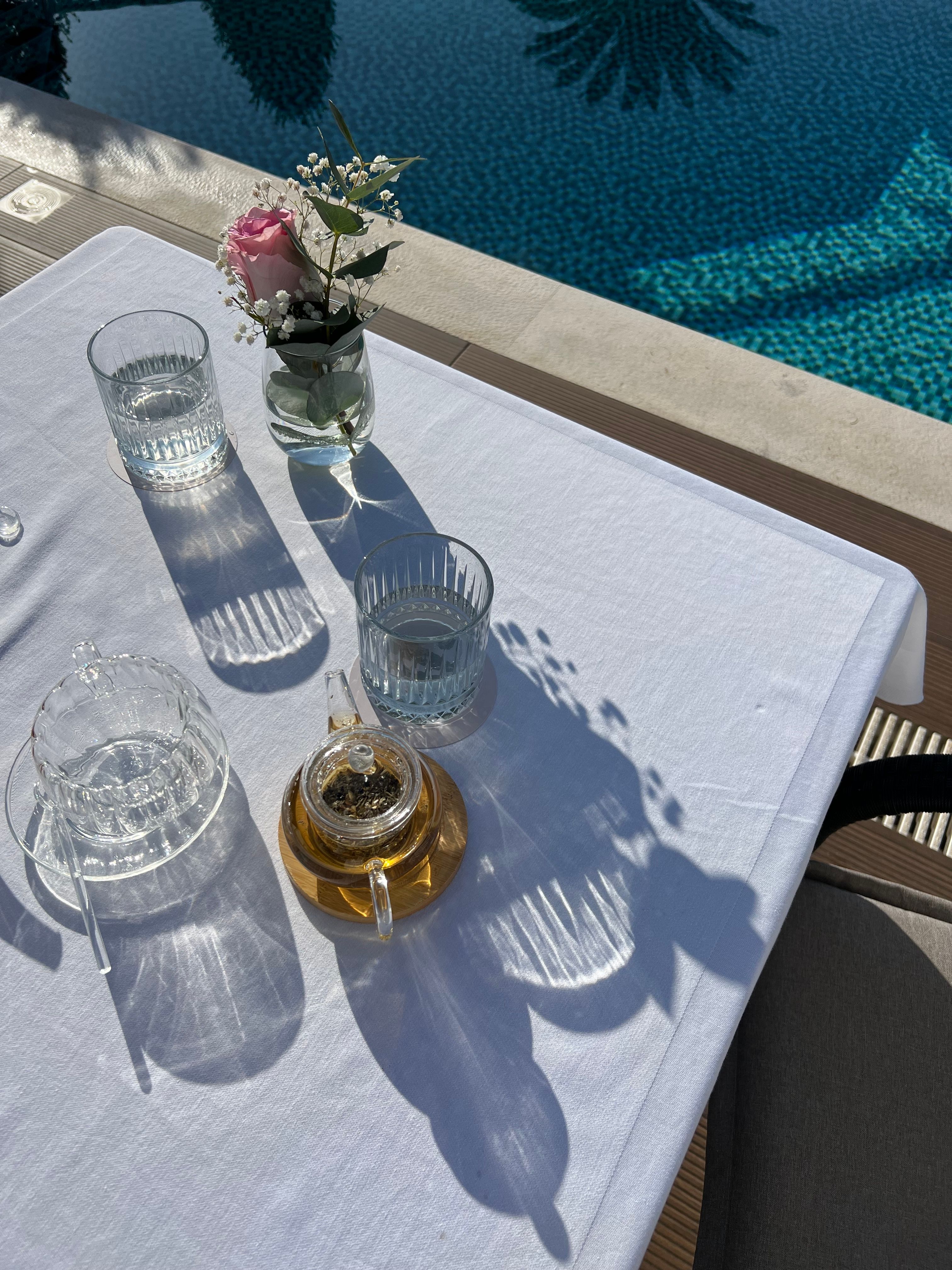 Elegant poolside setup with a teapot, glasses, and flower vase on a sunny day in Montenegro.
