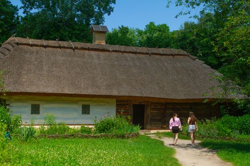 Free Two women walking towards a traditional thatched roof cottage surrounded by greenery. Stock Photo