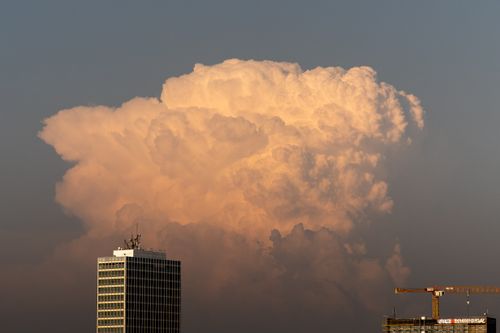 Free A towering cumulonimbus cloud illuminated by sunset over buildings in Düsseldorf, symbolizing urban nature contrast. Stock Photo