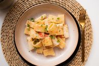 From above of juicy pasta with tiny slices of tomato and chopped parsley with ground black pepper on round plate near fork on straw mat