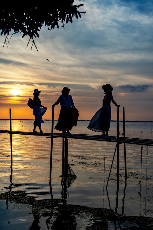 Free Three silhouetted figures on a lakeside dock at sunset create a serene landscape. Stock Photo