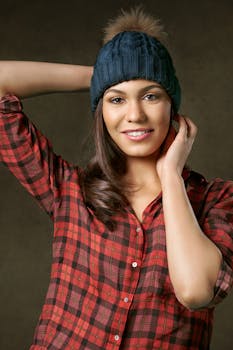 一位面带微笑、身穿红色格子衬衫、头戴针织无檐帽的女子，在室内自信地摆着姿势