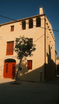 Elegant Mediterranean villa exterior with arched windows and tree casting shadow.