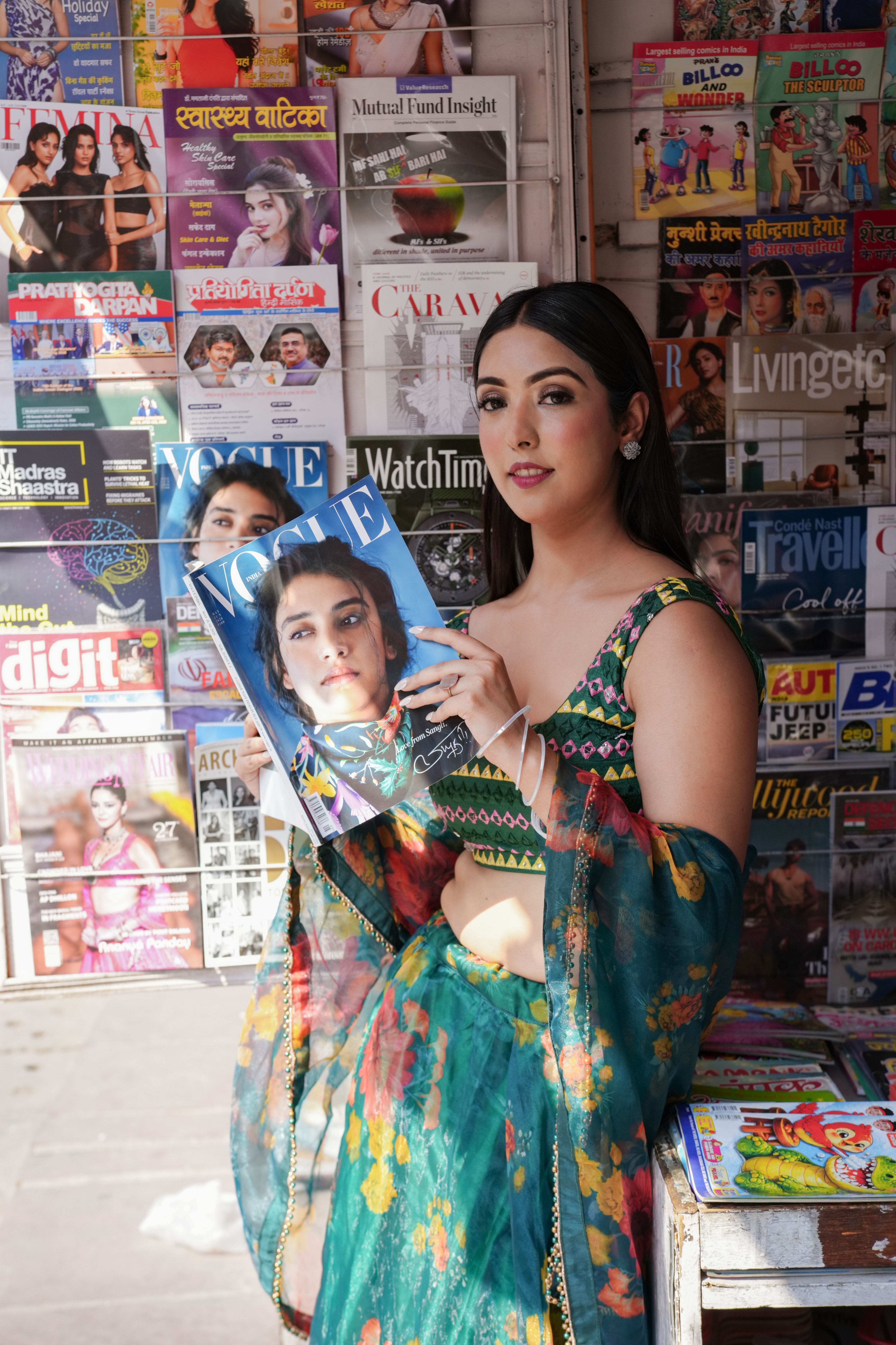 Young woman holding a fashion magazine at a colorful newsstand full of various publications.