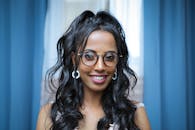 一位戴眼镜、留着深色长发、微笑的女人的肖像，室内挂着蓝色窗帘