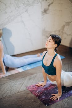 Two women performing yoga poses indoors, focusing on relaxation and wellness.