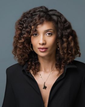 Stylish portrait of a woman wearing a black outfit, with curly hair and pendant necklace.
