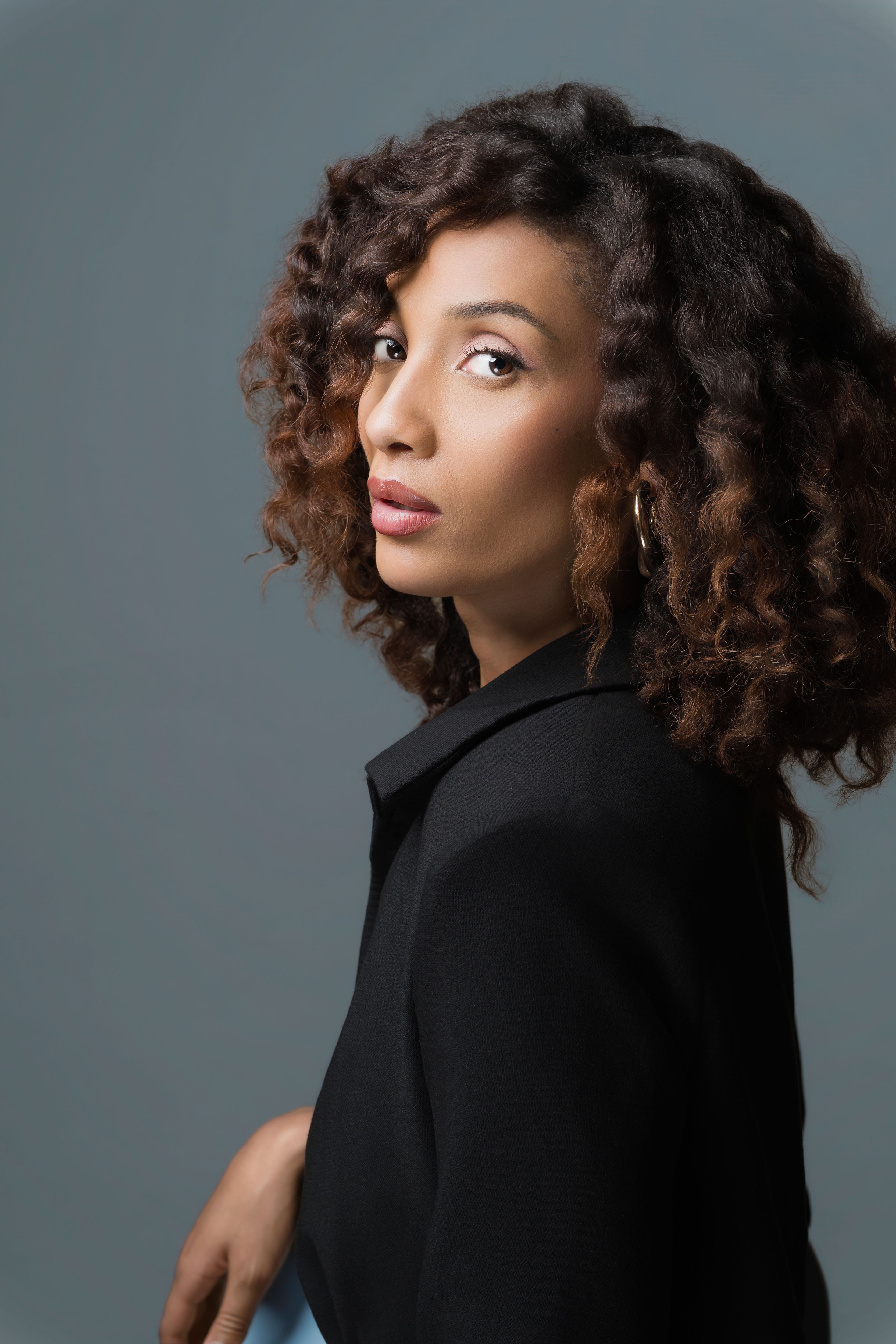 Stylish portrait of a young woman with curly hair in a studio setting, showcasing elegance and sophistication.