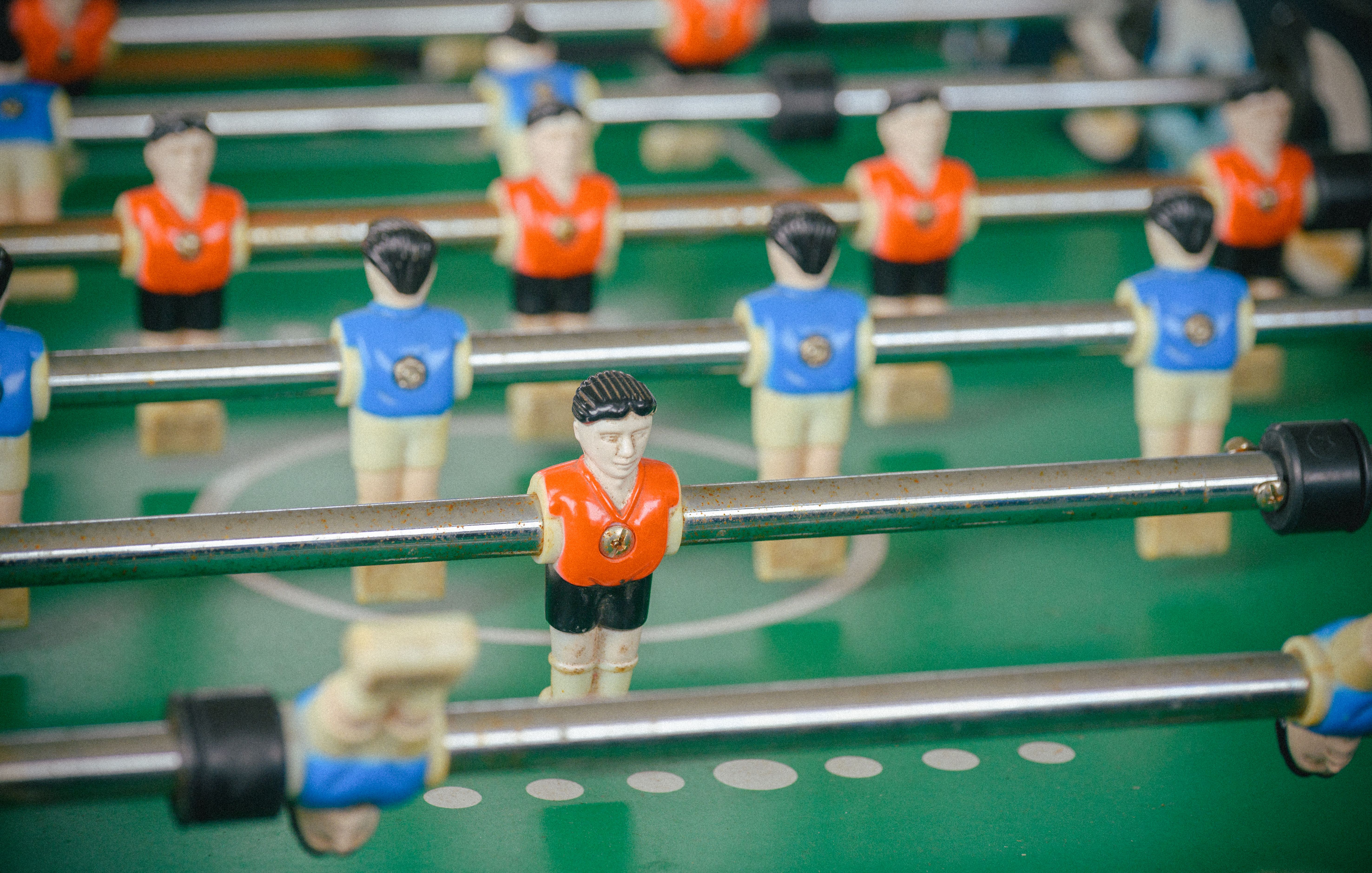 Detailed view of a foosball table with figures in orange and blue jerseys during gameplay.