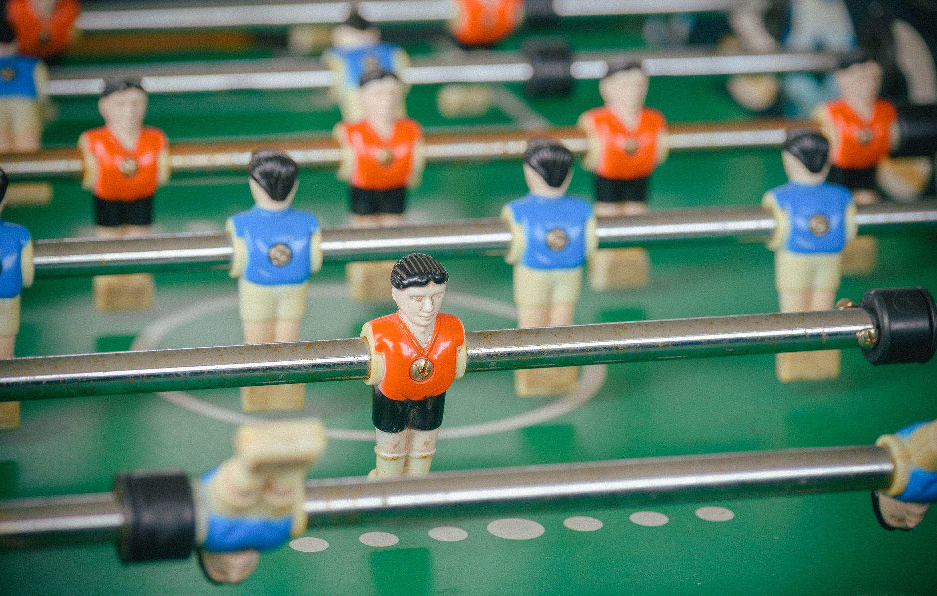 Detailed view of a foosball table with figures in orange and blue jerseys during gameplay.