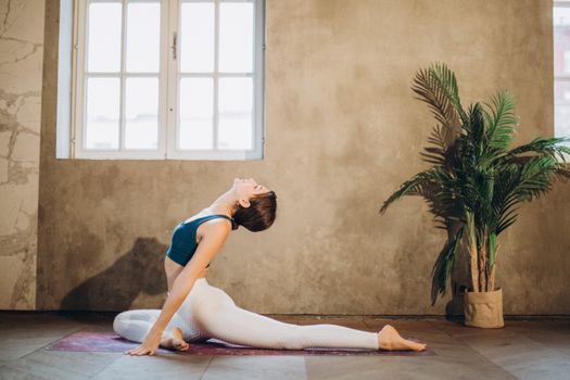 Woman performing yoga in Ardha Kapotasana indoors, emphasizing relaxation and flexibility.