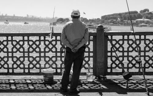 Free Senior man fishing from a bridge overlooking water, with boats in the distance. Black and white mood. Stock Photo