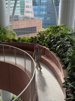 Man walking on a curved urban pathway with lush plants in a city environment.