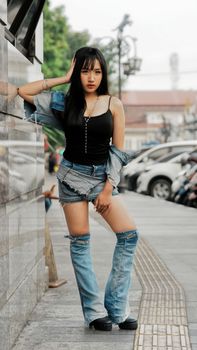 Young woman poses stylishly in denim attire on a street in Bandung, Indonesia.