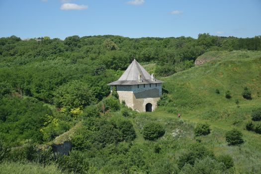 A historic stone building with a pyramid roof in a lush green landscape during a sunny day.