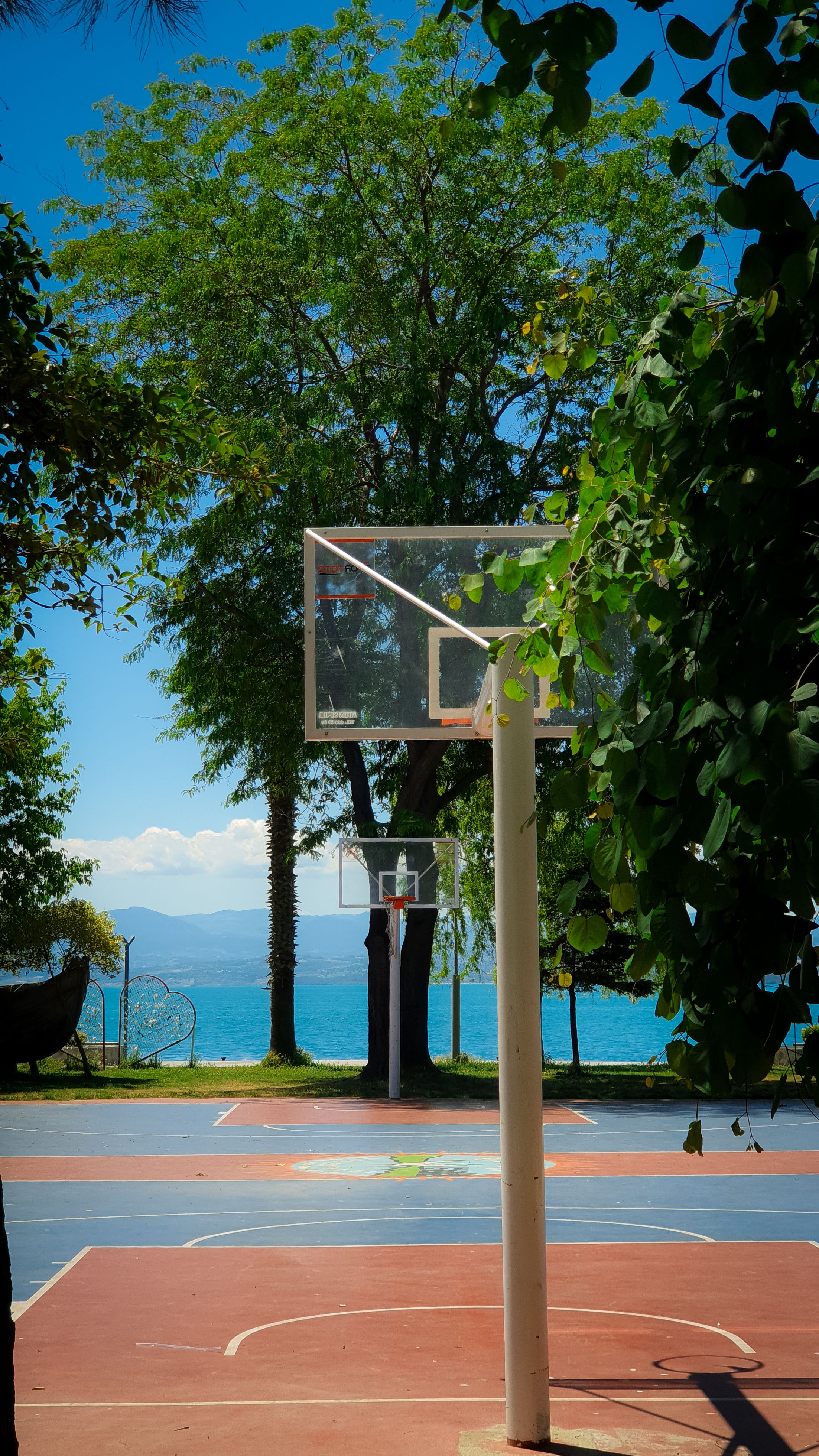 A scenic basketball court near a beach surrounded by trees on a clear day.