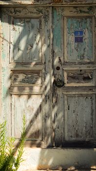 Weathered wooden door with peeling paint and vintage style casting shadows in sunlight.