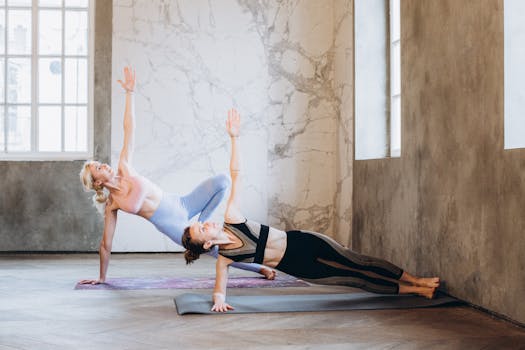 Two women performing yoga side plank pose indoors, focusing on balance and strength.