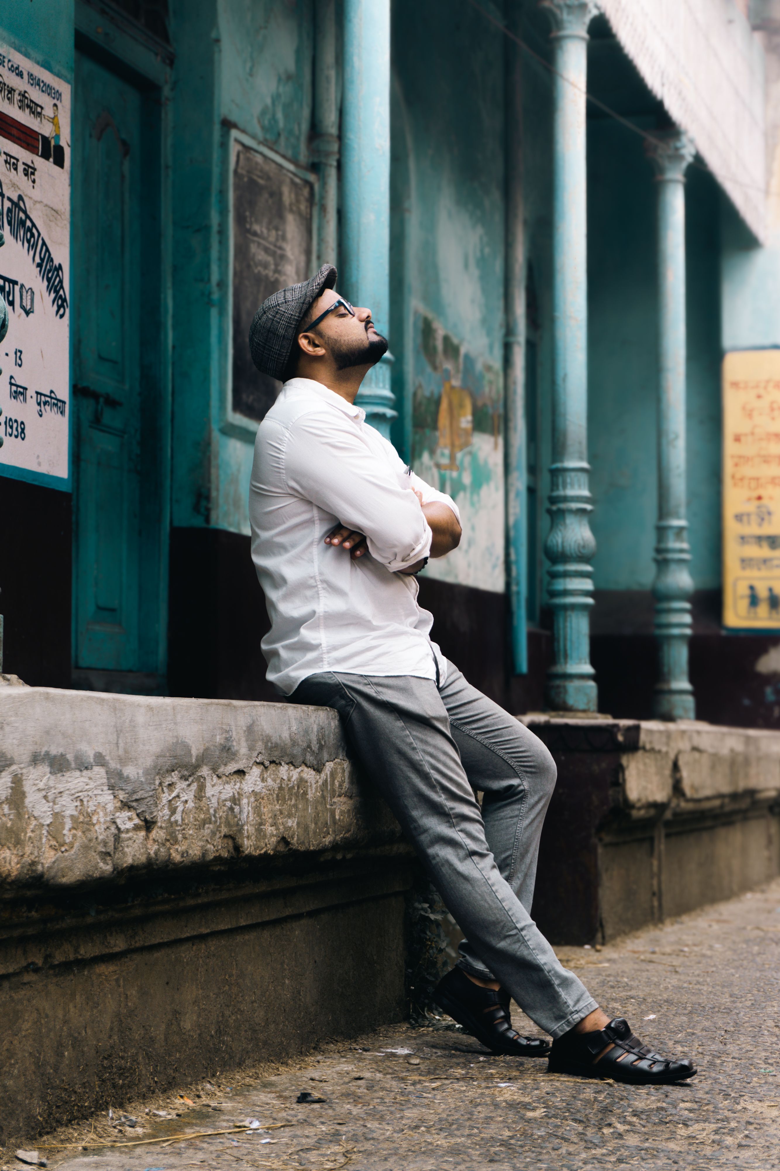 Man in casual attire leaning against a wall, looking thoughtful in an urban setting.